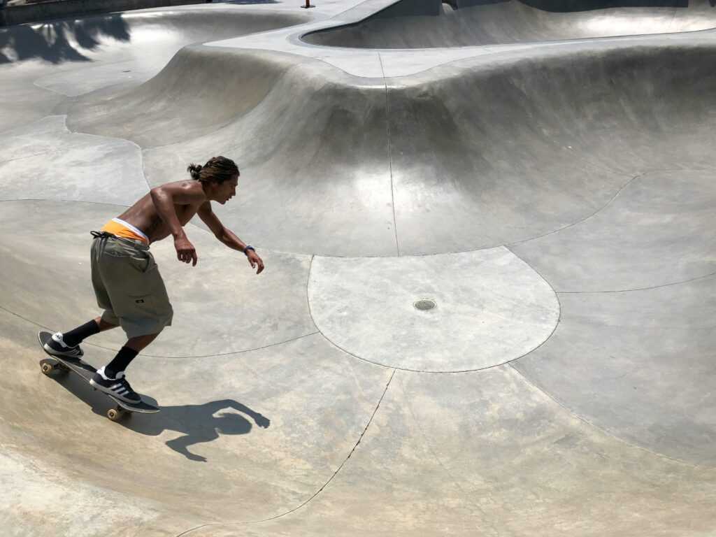 Young man skateboarding in a sunlit concrete skatepark, showcasing agility and style.